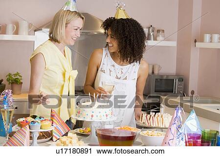 Stock Image - Two women at party standing by food table smiling. Fotosearch