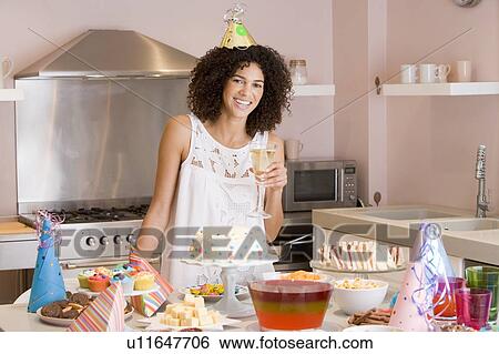 Stock Photograph - Woman at party holding drink standing by food table smiling. Fotosearch