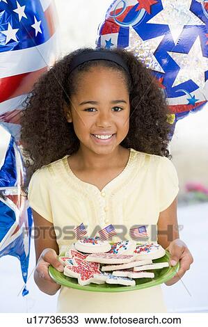 Stock Image - Young girl on fourth of July with balloons and cookies smiling. Fotosearch