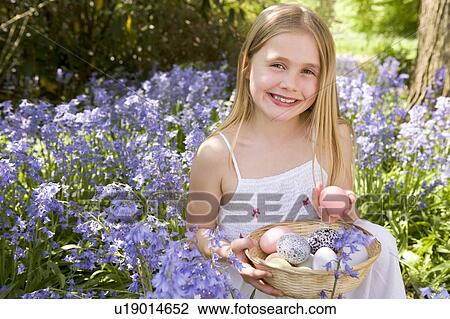 Stock Image - Young girl outdoors holding various eggs in basket smiling. Fotosearch
