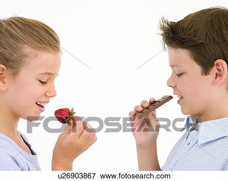 Stock Photo - Sister eating strawberry by brother eating chocolate bar. Fotosearch