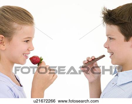 Stock Photograph - Sister eating strawberry by brother eating chocolate bar. Fotosearch