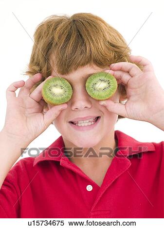 Stock Photography - Young boy holding kiwi halves over eyes smiling. Fotosearch