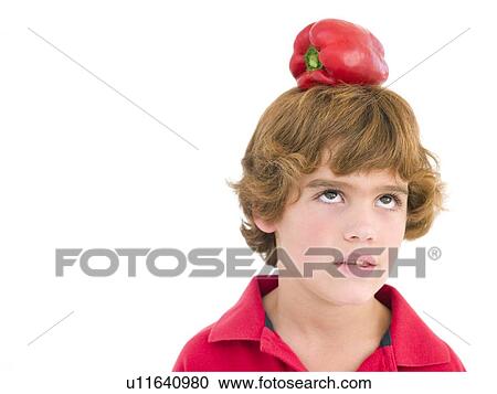 Stock Image - Young boy with red pepper on his head frowning. Fotosearch