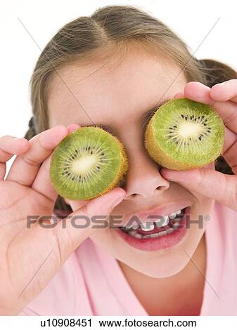 Young girl holding kiwi halves over eyes smiling View Large Photo Image Stock Image - Young girl holding kiwi halves over eyes smiling. Fotosearch