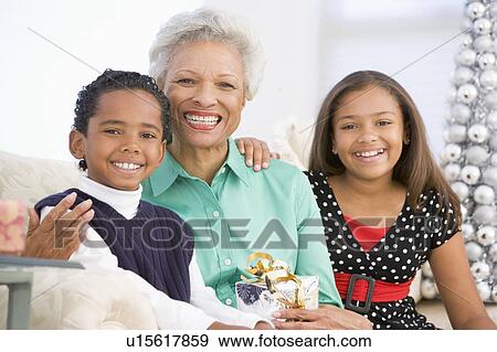 Grandmother Sitting With Her Two Grandchildren, Holding A Christmas Gift View Large Photo Image Stock Photo - Grandmother Sitting With Her Two Grandchildren, Holding A Christmas Gift. Fotosearch