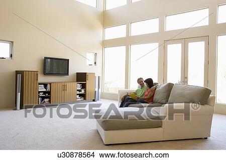 Picture - Couple reading book in living room smiling. Fotosearch