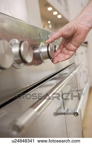 Stock Image - Hand on stove dial in kitchen. Fotosearch