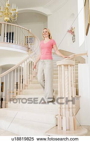 Stock Photography - Woman coming down staircase in luxurious home smiling. Fotosearch