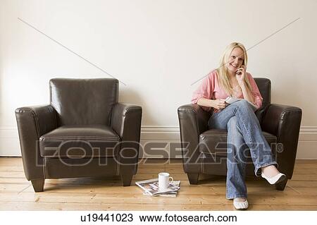 Woman sitting in chair with magazine on cellular phone smiling View Large Photo Image Stock Image - Woman sitting in chair with magazine on cellular phone smiling. Fotosearch