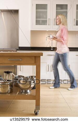 Woman walking in kitchen holding coffee View Large Photo Image Stock Photo - Woman walking in kitchen holding coffee. Fotosearch