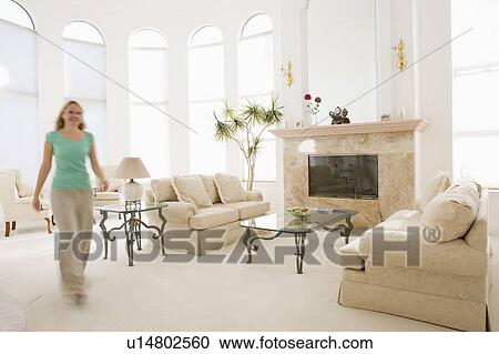Stock Image - Woman walking through living room. Fotosearch