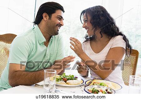 Stock Photography - Couple sitting at dinner table smiling (high key). Fotosearch