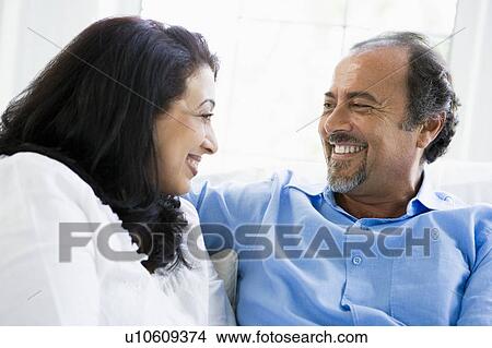 Picture - Couple sitting in living room smiling (high key). Fotosearch