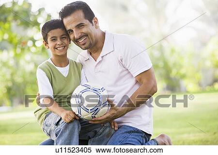 Stock Photography - Father and son outdoors in park with ball smiling (selective focus). Fotosearch