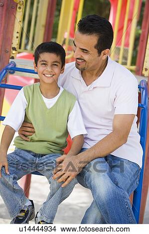 Father and son sitting on playground structure smiling (selective focus) View Large Photo Image Picture - Father and son sitting on playground structure smiling (selective focus). Fotosearch