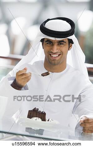Picture - Man at restaurant eating dessert and smiling (selective focus). Fotosearch