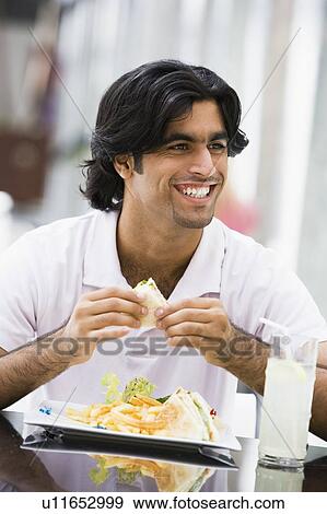 Stock Photo - Man at restaurant eating sandwich and smiling (selective focus). Fotosearch