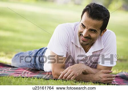 Man lying outdoors at park smiling (selective focus) View Large Photo Image Picture - Man lying outdoors at park smiling (selective focus). Fotosearch