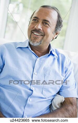 Stock Photography - Man sitting in living room smiling (high key/selective focus). Fotosearch