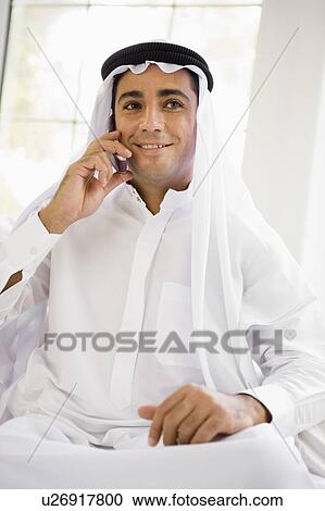 Stock Image - Man sitting indoors on cellular phone smiling (high key). Fotosearch