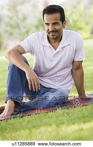 Stock Photo - Man sitting outdoors at park smiling (selective focus). Fotosearch