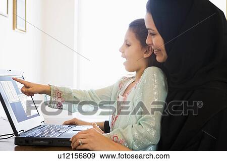 Stock Photo - Mother and daughter in office with laptop pointing and smiling (high key/selective focus) . Fotosearch