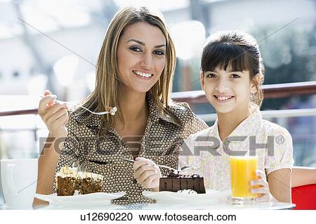 Stock Image - Mother at restaurant with daughter girl eating dessert and smiling (selective focus). Fotosearch