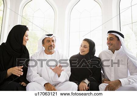 Stock Image - Two couples sitting in living room talking and smiling (high key/selective focus). Fotosearch