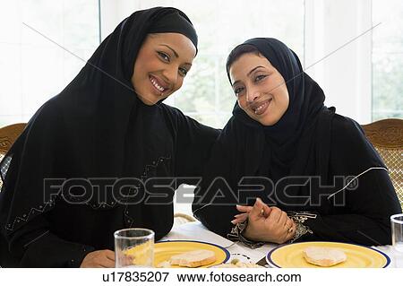 Stock Photo - Two women sitting at dinner table smiling (high key). Fotosearch