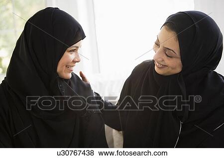 Stock Photo - Two women sitting indoors talking and smiling (high key). Fotosearch