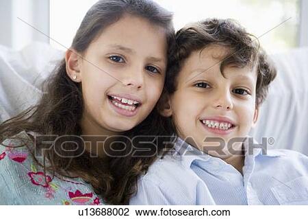 Stock Image - Two young children in living room smiling (high key). Fotosearch