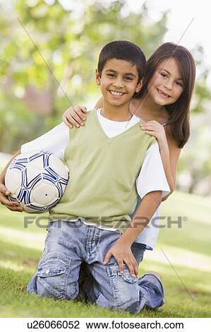 Stock Image - Two young children outdoors in park with ball smiling (selective focus). Fotosearch