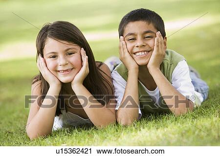 Stock Image - Two young children outdoors lying in park smiling (selective focus). Fotosearch