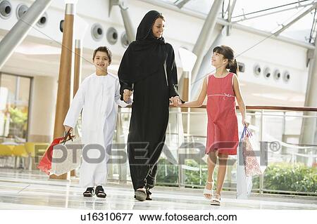Woman and two young children walking in mall holding hands and smiling (selective focus) View Large Photo Image Stock Photo - Woman and two young children walking in mall holding hands and smiling (selective focus). Fotosearch