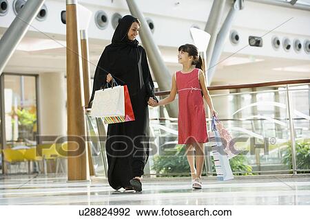 Stock Image - Woman and young girl walking in mall smiling (selective focus). Fotosearch