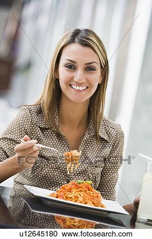 Stock Image - Woman at restaurant eating spaghetti and smiling (selective focus). Fotosearch