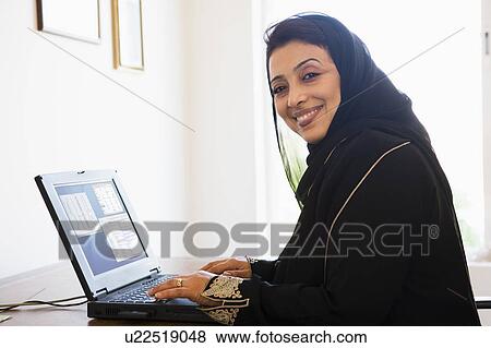Stock Photo - Woman in office with laptop smiling (high key/selective focus). Fotosearch