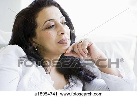 Stock Image - Woman sitting in living room thinking (high key). Fotosearch