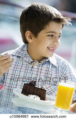 Stock Image - Young boy at restaurant eating dessert and smiling (selective focus). Fotosearch