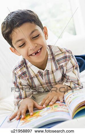 Stock Photo - Young boy in living room reading a book and smiling (high key). Fotosearch