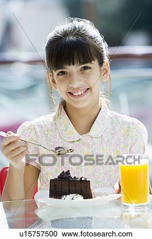 Stock Image - Young girl at restaurant eating dessert and smiling (selective focus). Fotosearch
