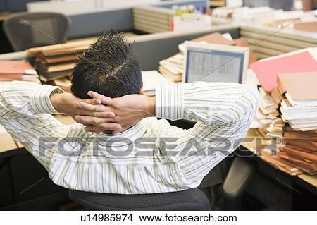 Picture - Businessman in cubicle with laptop and stacks of files. Fotosearch