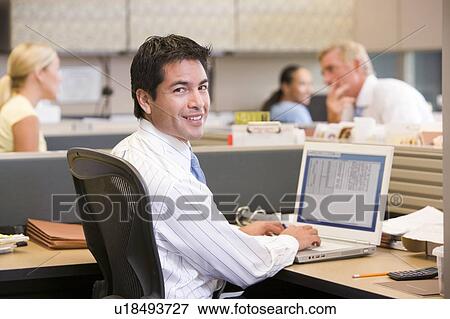 Businessman in cubicle with laptop smiling View Large Photo Image Stock Photo - Businessman in cubicle with laptop smiling. Fotosearch