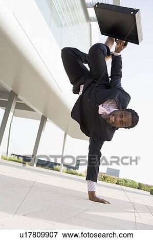 Stock Photo - Businessman outdoors by building standing on one hand smiling. Fotosearch