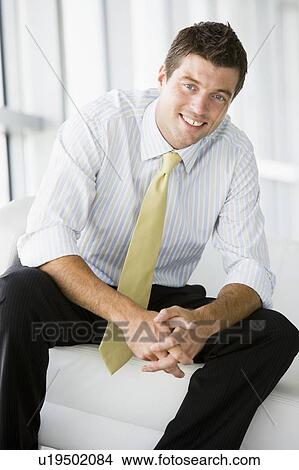 Picture - Businessman sitting in office lobby smiling. Fotosearch