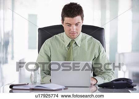 Picture - Businessman sitting in office with personal organizer and laptop. Fotosearch