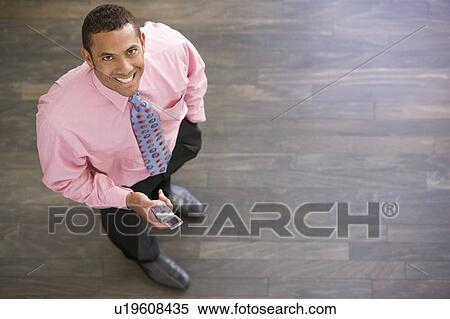 Businessman standing indoors with cellular phone smiling View Large Photo Image Stock Photography - Businessman standing indoors with cellular phone smiling. Fotosearch