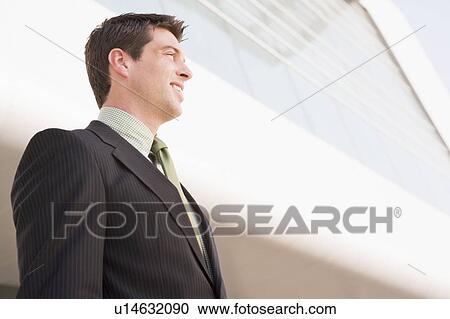 Stock Image - Businessman standing outdoors by building smiling. Fotosearch