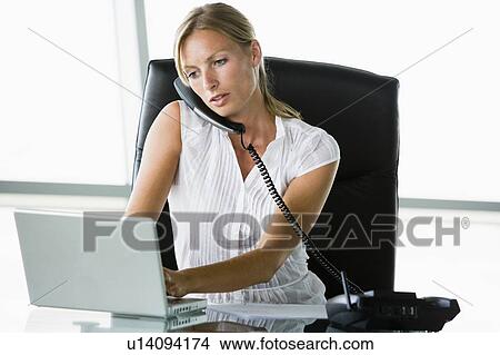 Businesswoman sitting in office with laptop on telephone View Large Photo Image Picture - Businesswoman sitting in office with laptop on telephone. Fotosearch